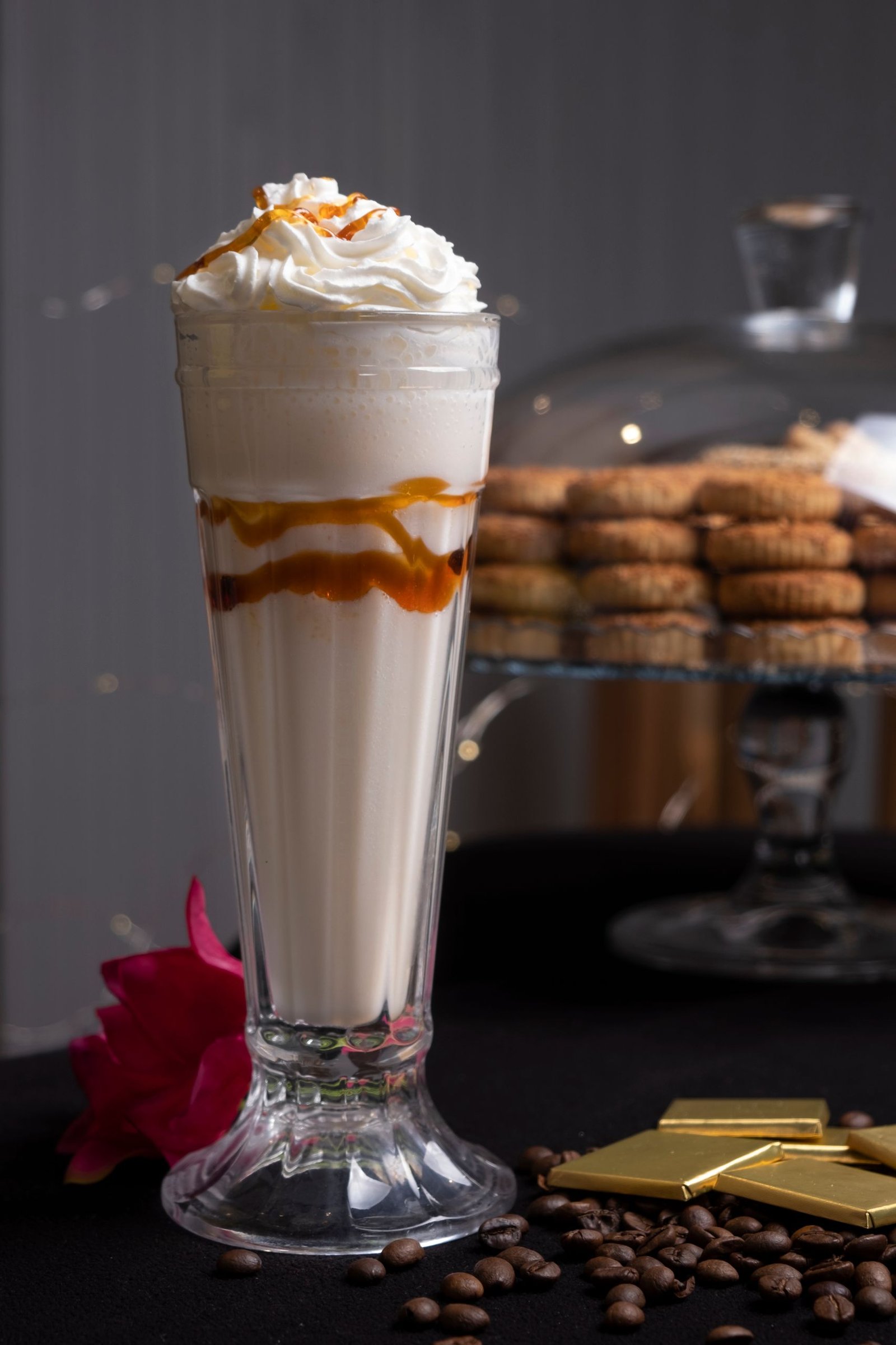 A mouthwatering vanilla milkshake topped with whipped cream and caramel sauce, accompanied by cookies and coffee beans.