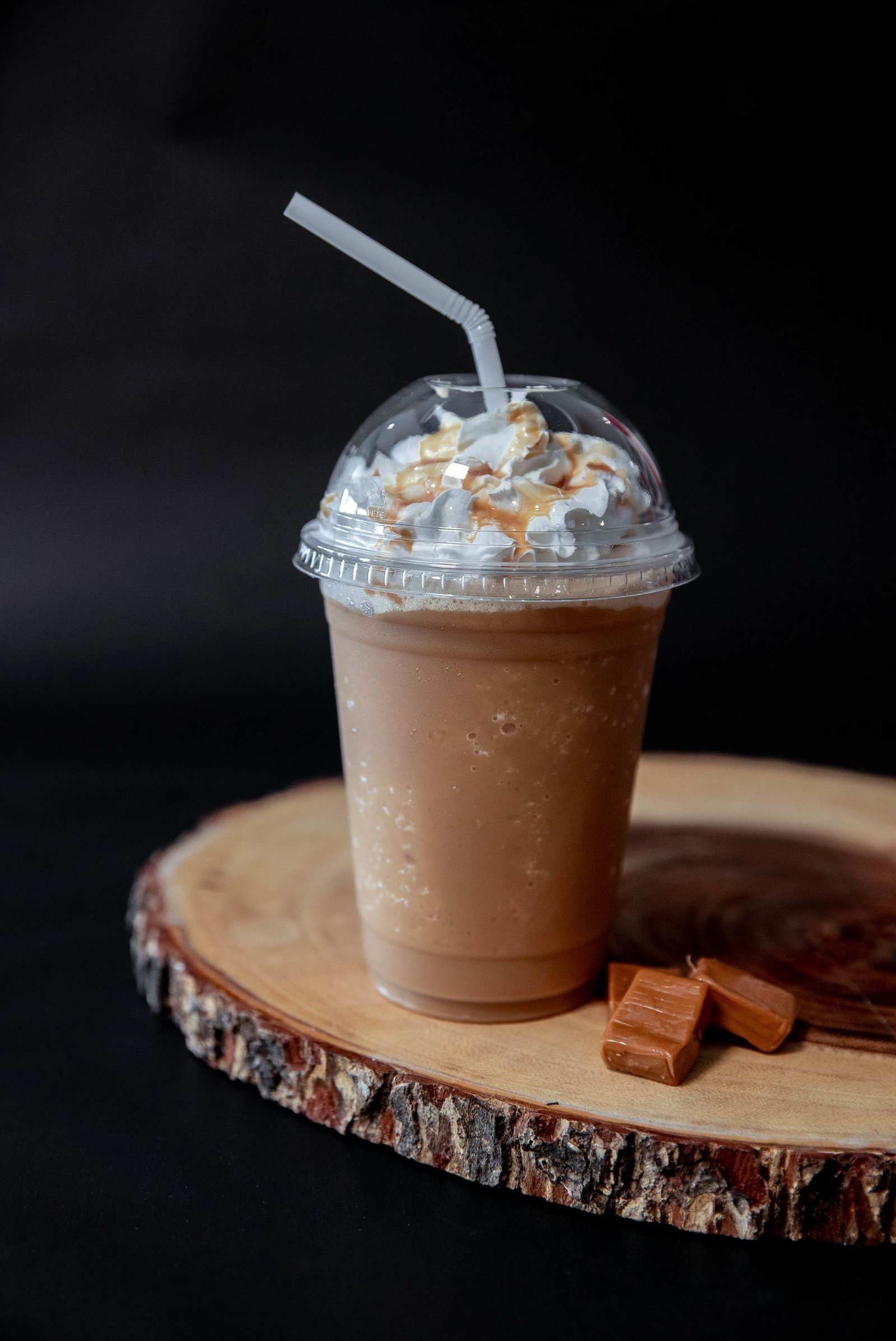 Indulgent caramel milkshake topped with whipped cream, served on a rustic wood slice.