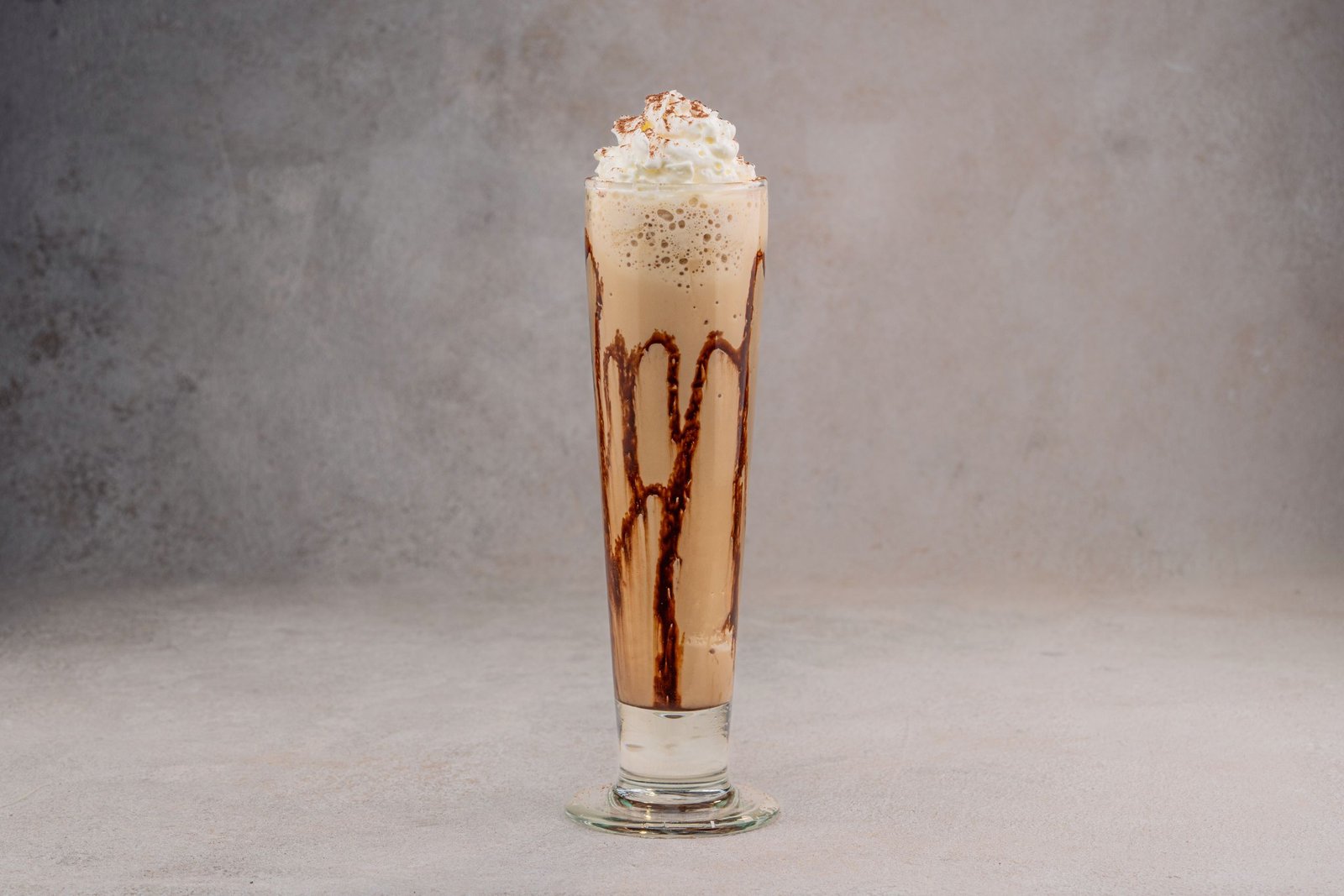Tall glass of chocolate milkshake topped with whipped cream on a gray background.